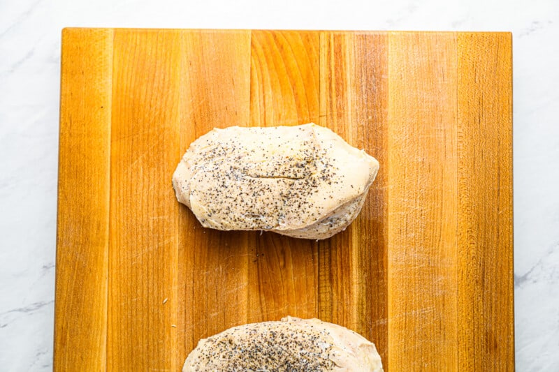 2 cooked sous vide chicken breasts on a wooden cutting board.