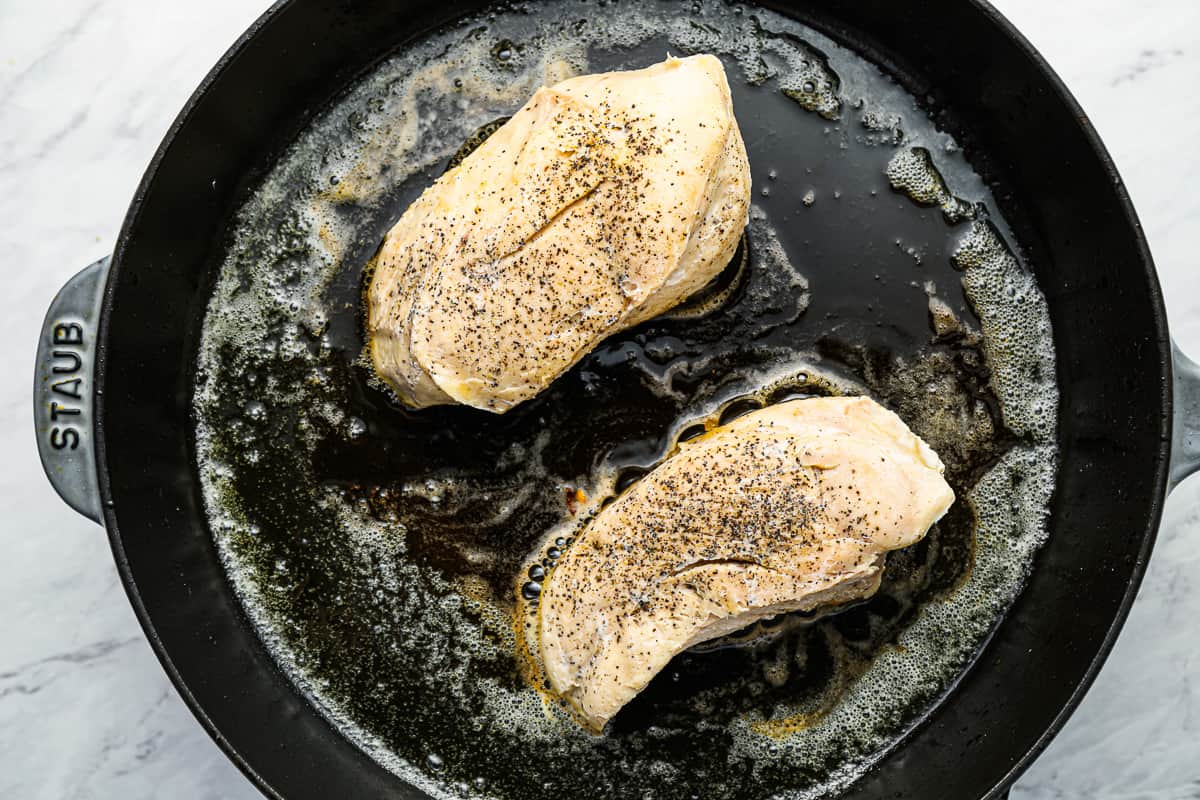 2 cooked sous vide chicken breasts searing in a cast iron pan.