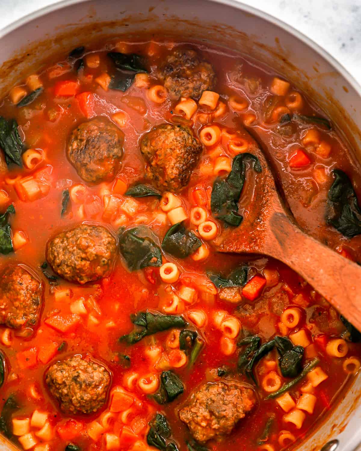 partial overhead view of Italian meatball soup cooking in a Dutch oven with a wooden spoon.