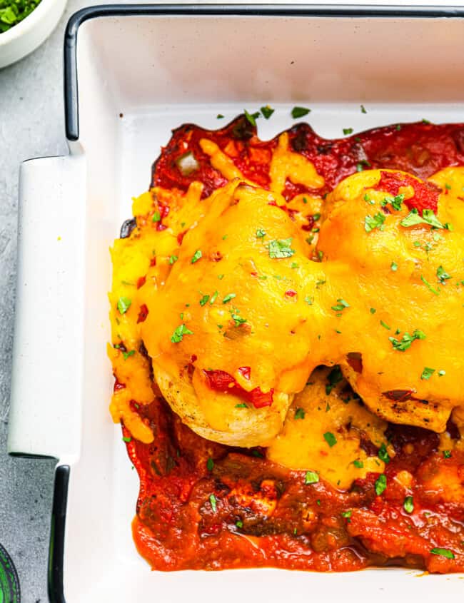 partial overhead view of baked salsa chicken in a white rectangular baking pan.