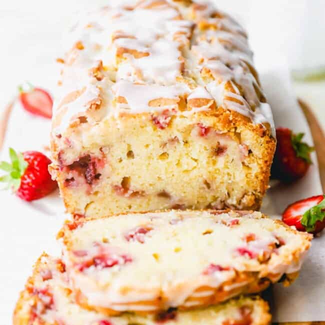 three-quarters view of sliced strawberry bread on parchment paper on a wooden cutting board with two slices laying in front of it.