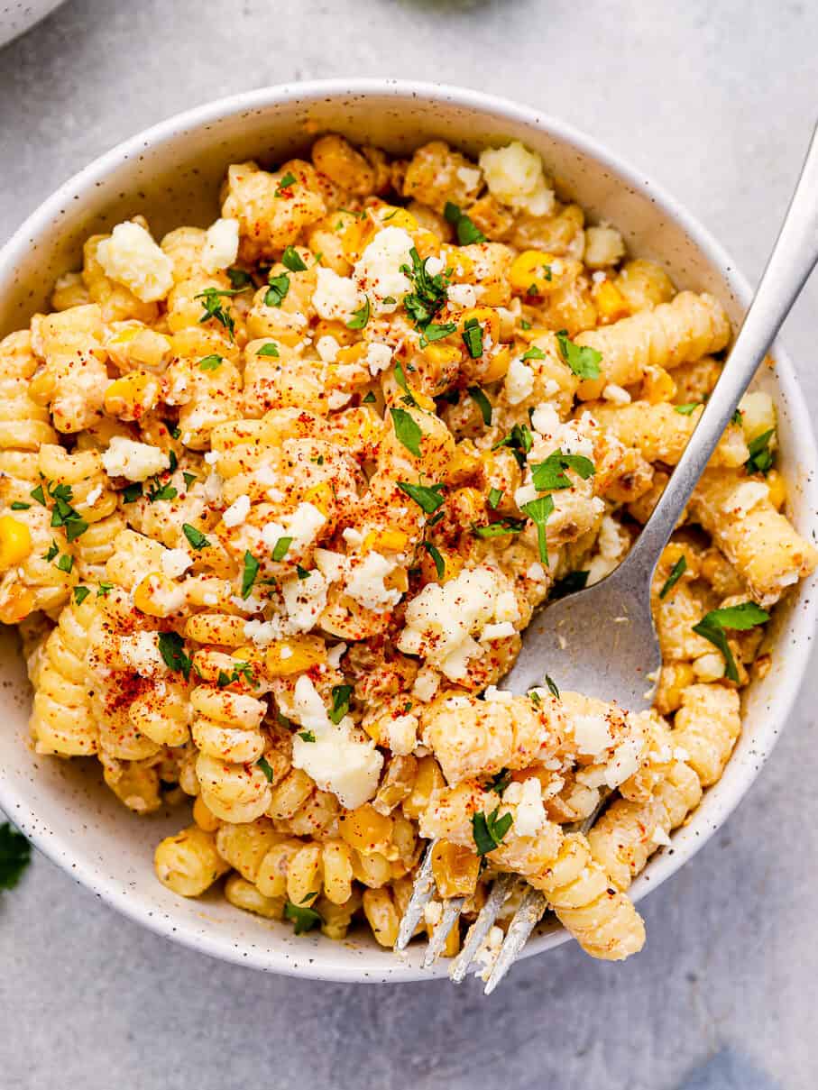 overhead view of a serving of street corn pasta salad in a white bowl with a fork.