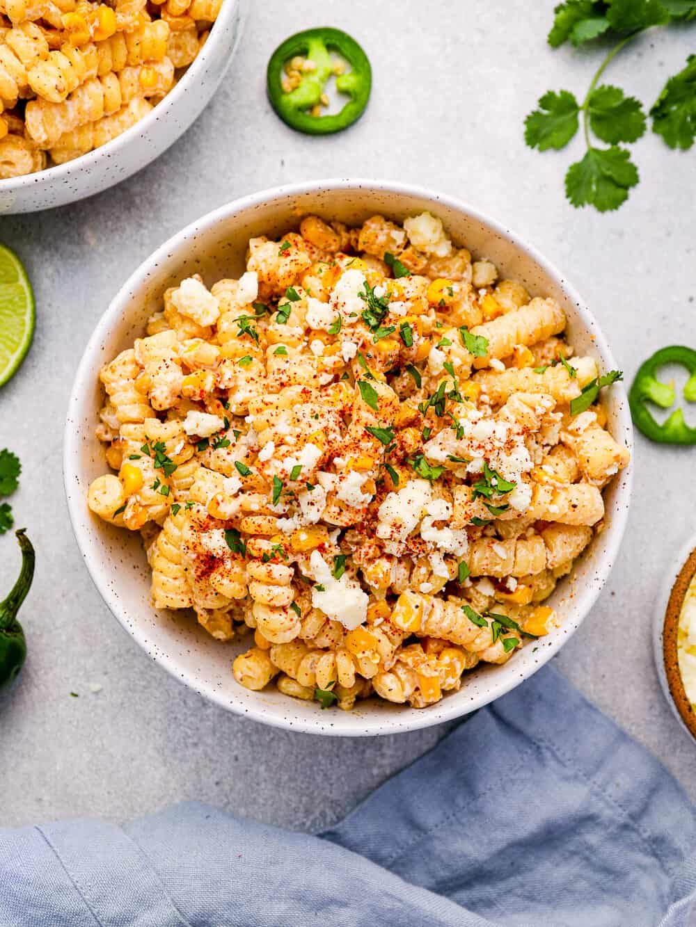 overhead view of a serving of street corn pasta salad in a white bowl surrounded by sliced jalapeños.