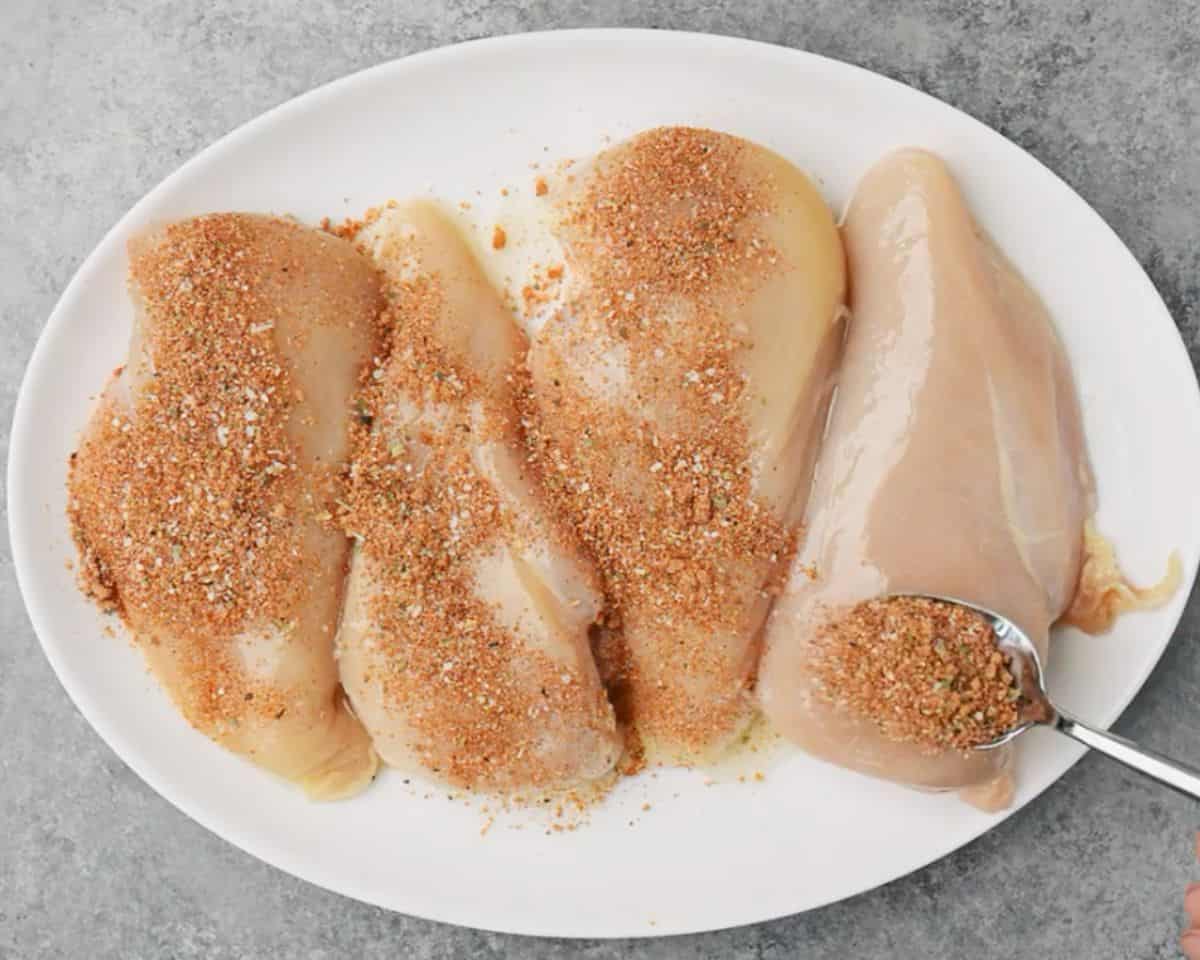 Raw chicken breasts on a platter being sprinkled with homemade spice rub before baking - 10