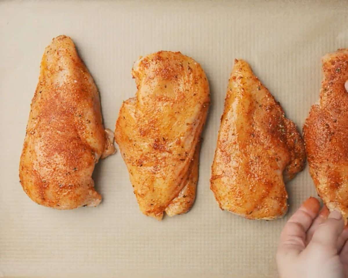 Seasoned chicken breasts arranged on a parchment lined sheet pan ready for the oven - 11