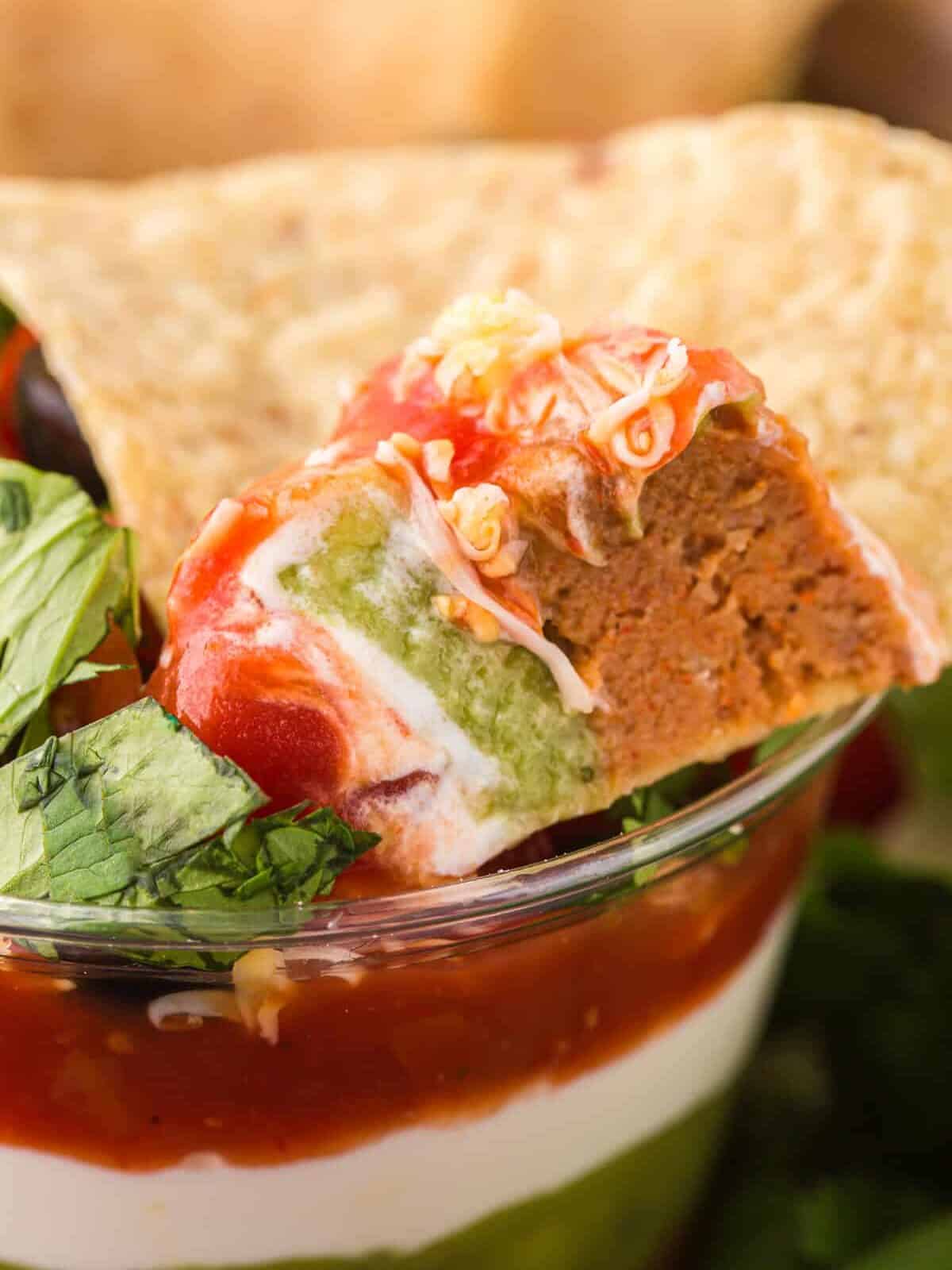 close up of a chip scooping 7 layer dip from a dip cup.