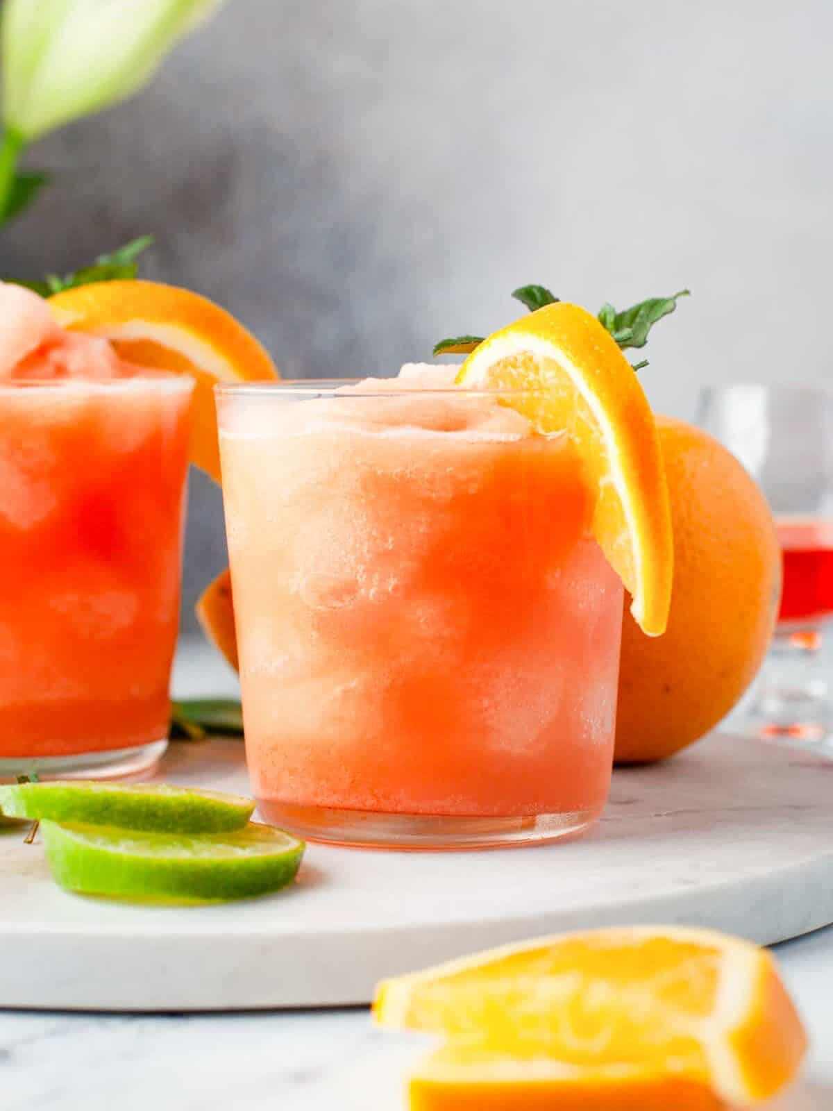 frozen Aperol margaritas in glasses with orange slice and mint garnishes