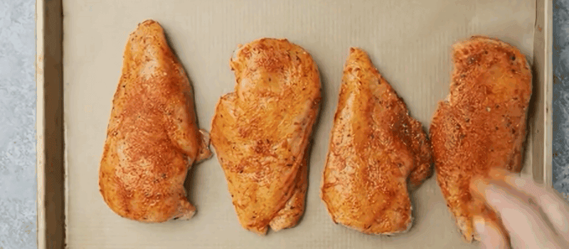 Chicken breasts on a parchment lined baking sheet.