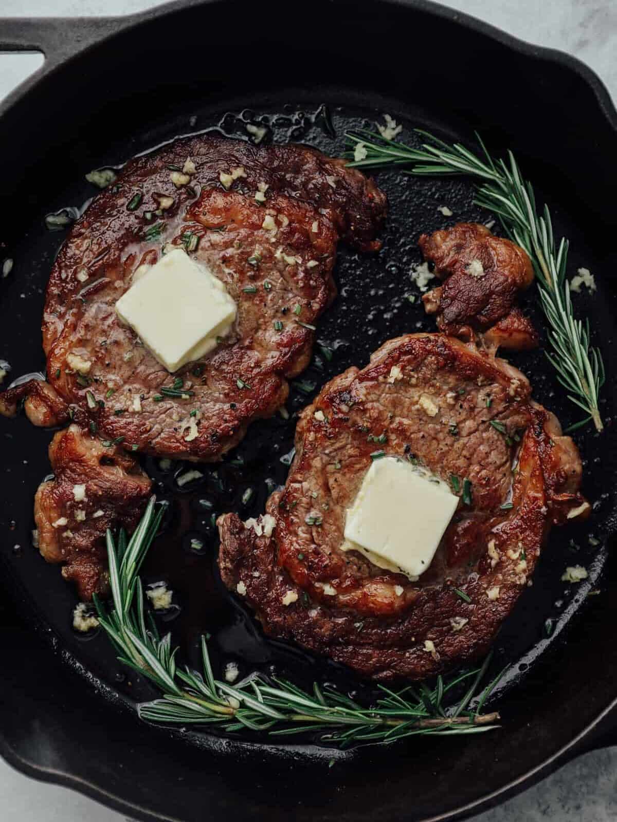 2 pan seared ribeye steaks in a cast iron pan with butter.