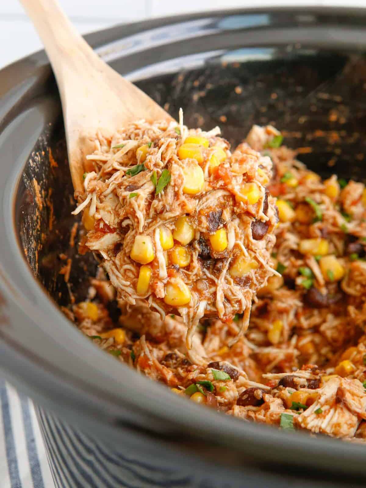 close up of crockpot mexican shredded chicken in a crockpot with a wooden spoon.