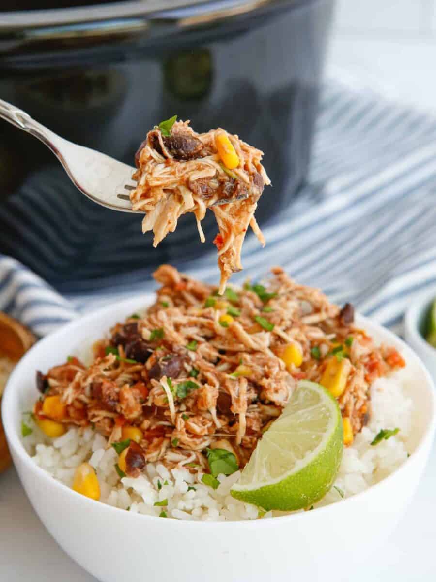 A forkful of crockpot Mexican shredded chicken over Mexican shredded chicken in a white bowl.