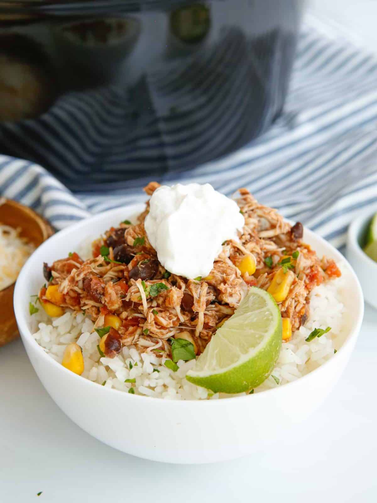 crockpot mexican shredded chicken over rice in a white bowl with sour cream.