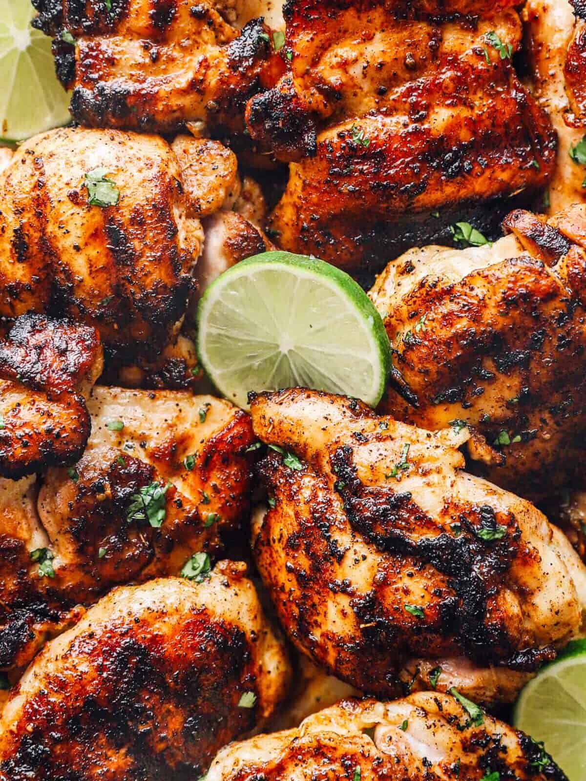 close up view of grilled chicken thighs with lime wedges.