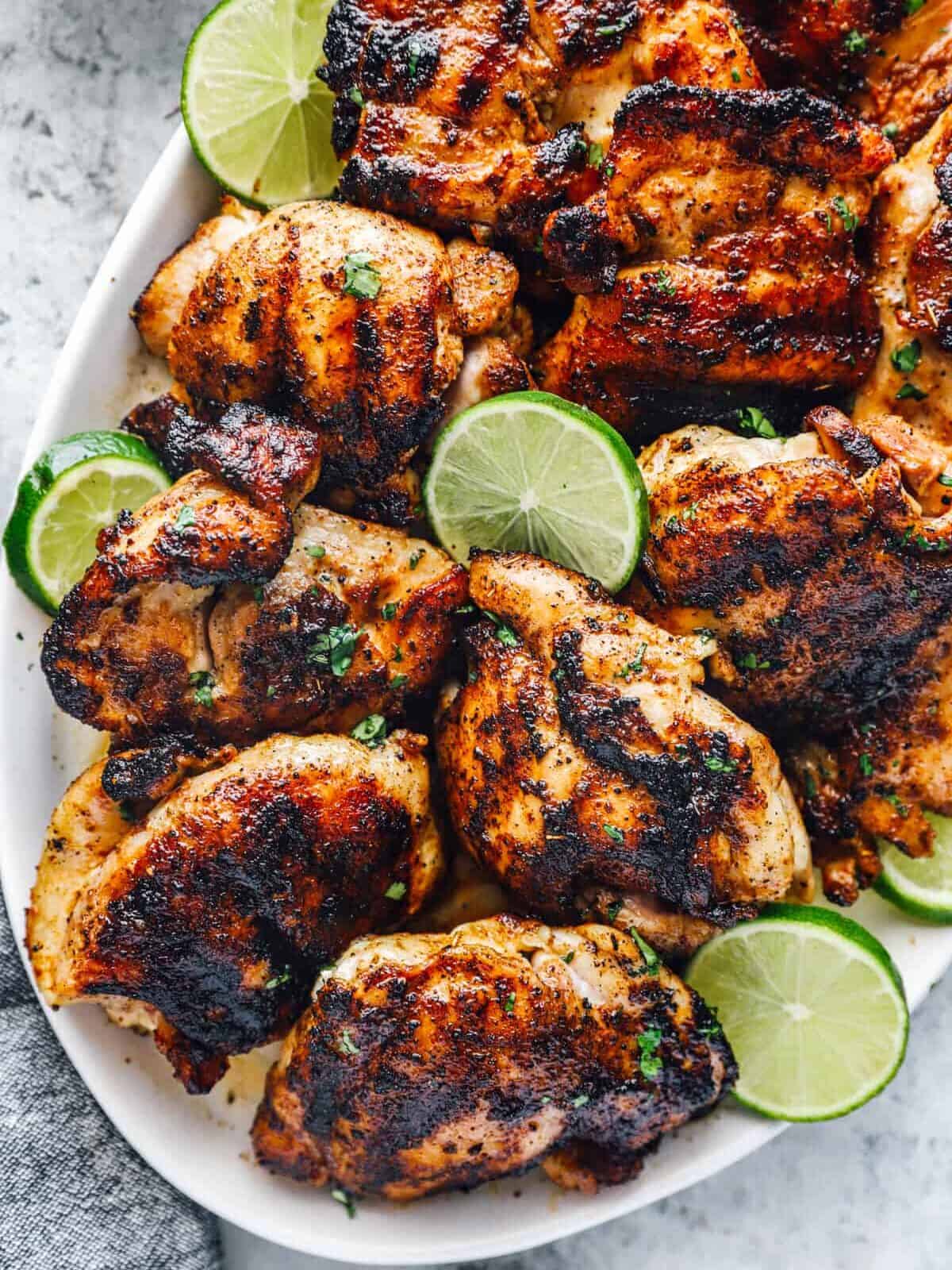 partial overhead view of seasoned chicken thighs on a white oval serving platter with lime slices.