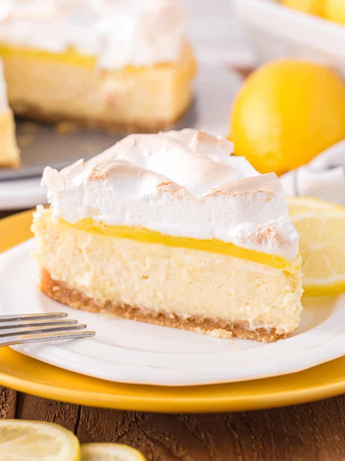 side view of a slice of lemon meringue cheesecake on a white plate.