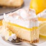 a partially eaten slice of lemon meringue cheesecake on a white plate with a fork.