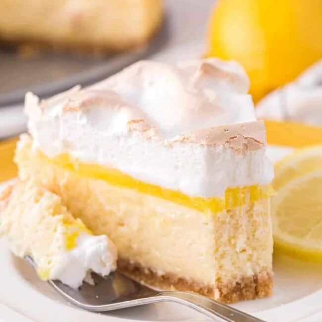 a partially eaten slice of lemon meringue cheesecake on a white plate with a fork.