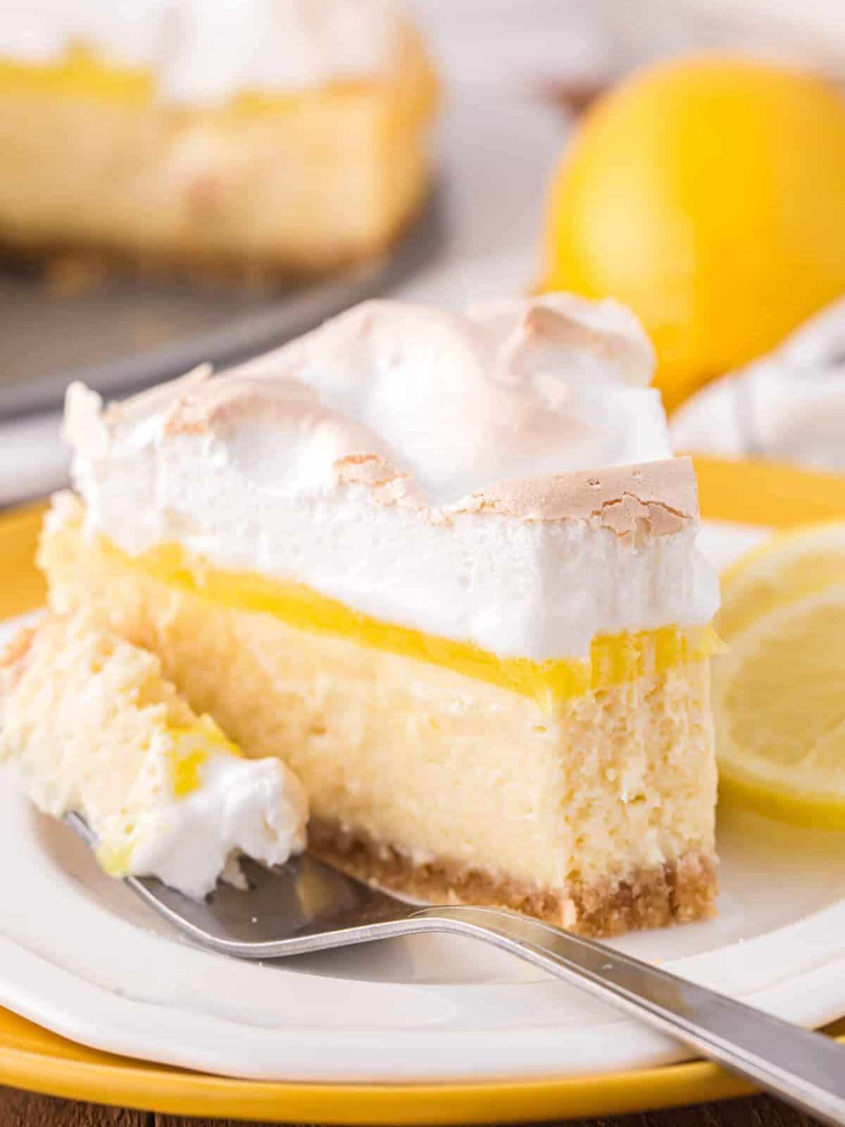 a partially eaten slice of lemon meringue cheesecake on a white plate with a fork.