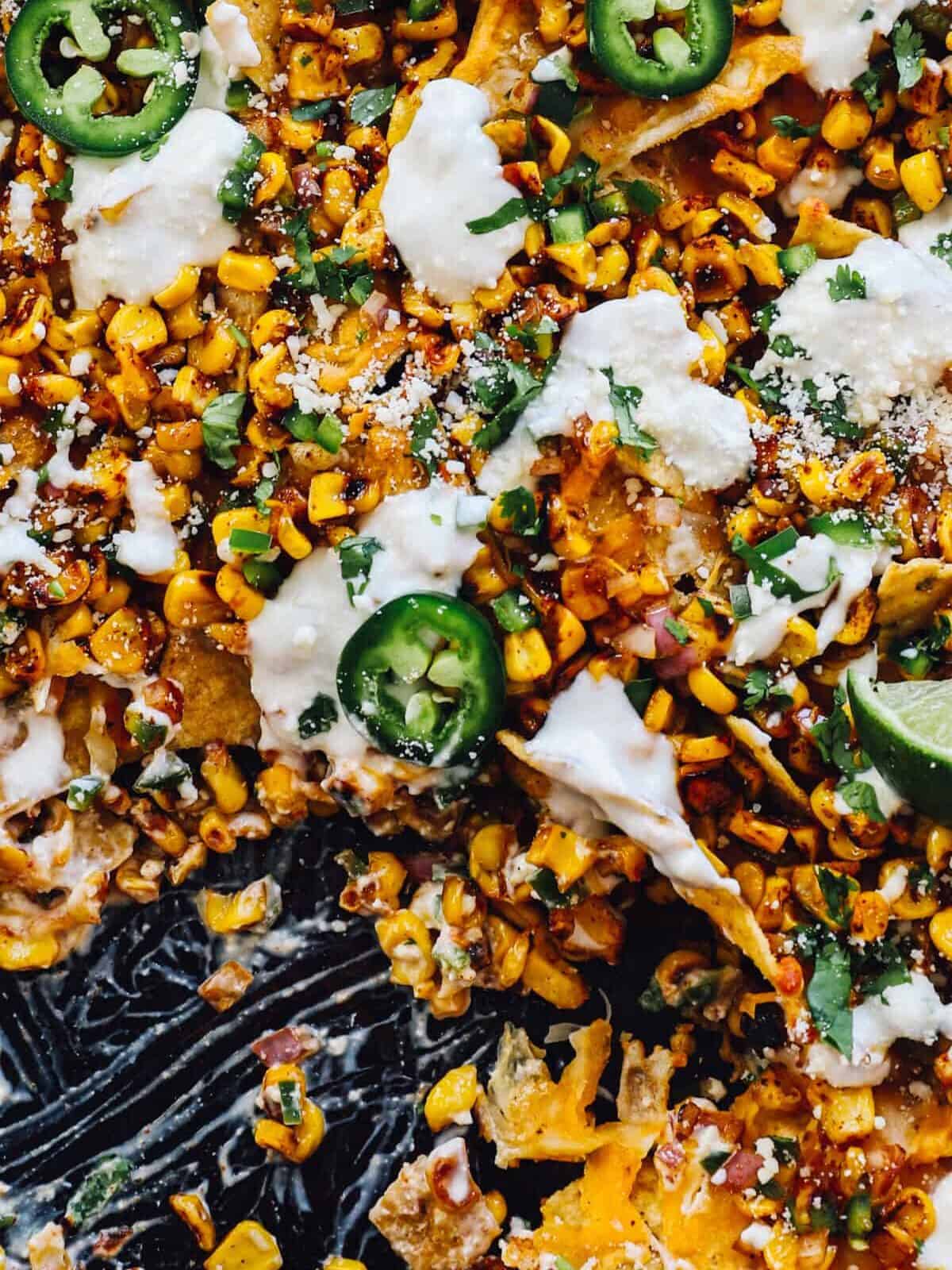 close up view of partially eaten street corn nachos on a baking sheet.