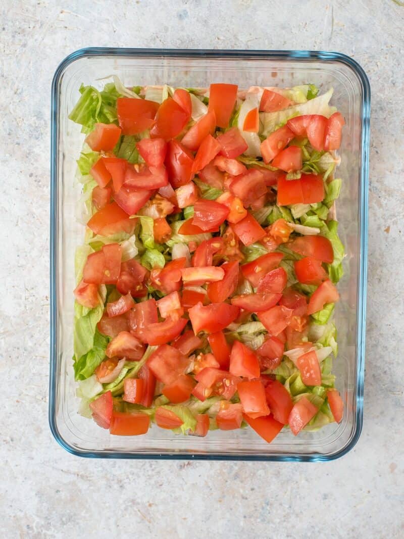 An overhead shot of fresh chopped lettuce and tomatoes on Layered Taco Dip.