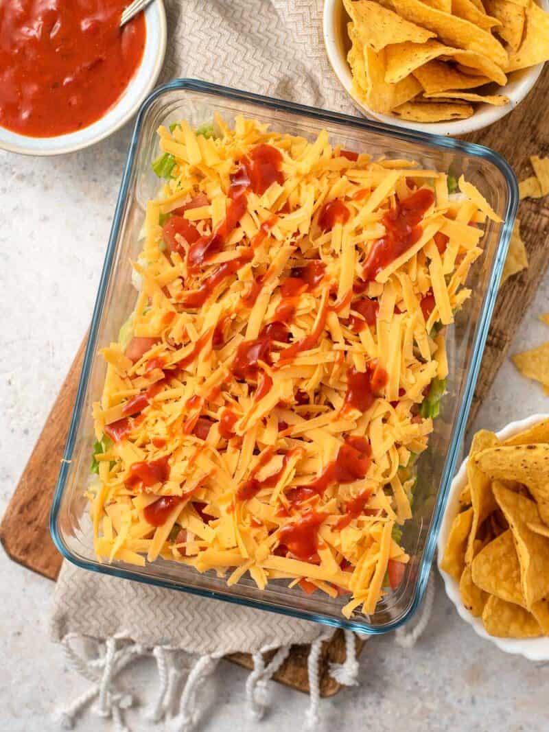 An overhead shot of a layered taco dip with shredded cheese and taco sauce