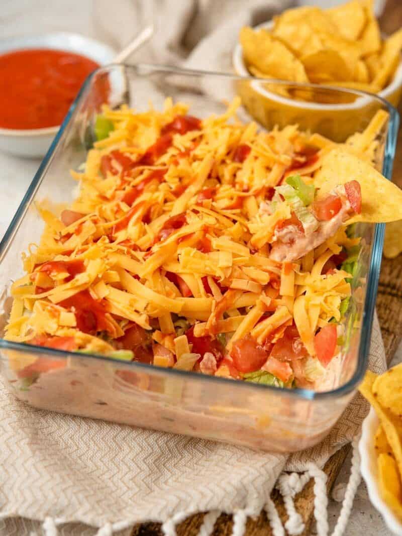 A close-up side shot of Layered Taco Dip with chips and taco sauce around it.