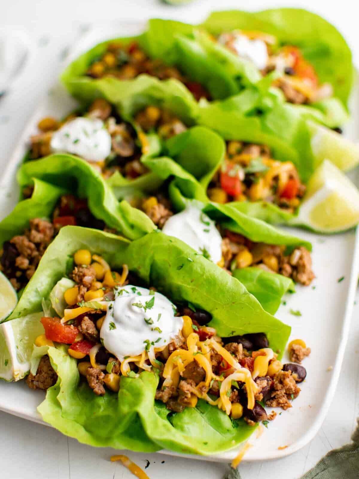 three-quarters view of taco lettuce wraps on a white rectangular serving platter.