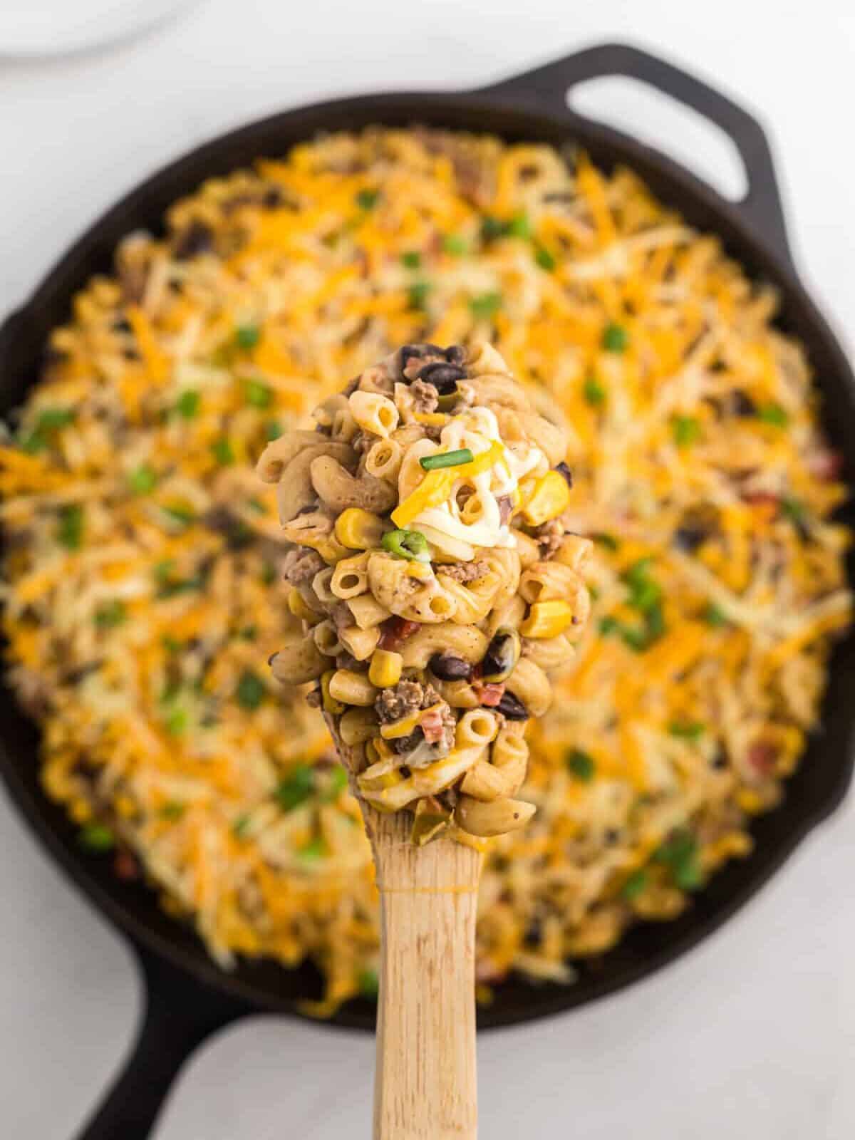 overhead view of taco mac and cheese in a cast iron pan with a wooden spoon.
