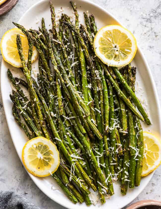 overhead view of air fryer asparagus on a white oval serving platter with lemon slices.
