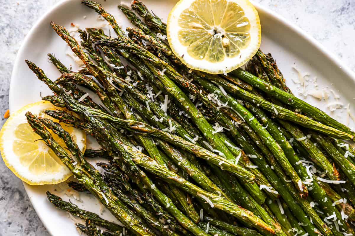close up overhead view of air fryer asparagus on an askew white oval serving platter with lemon slices.