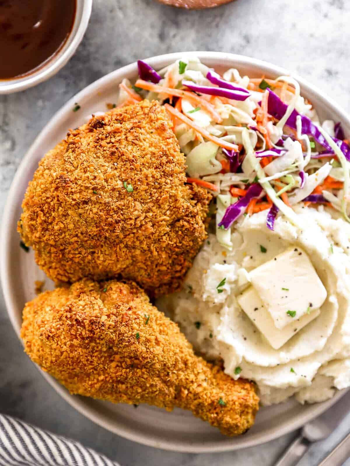 overhead view of 2 pieces of air fryer fried chicken on a white plate with mashed potatoes and coleslaw.