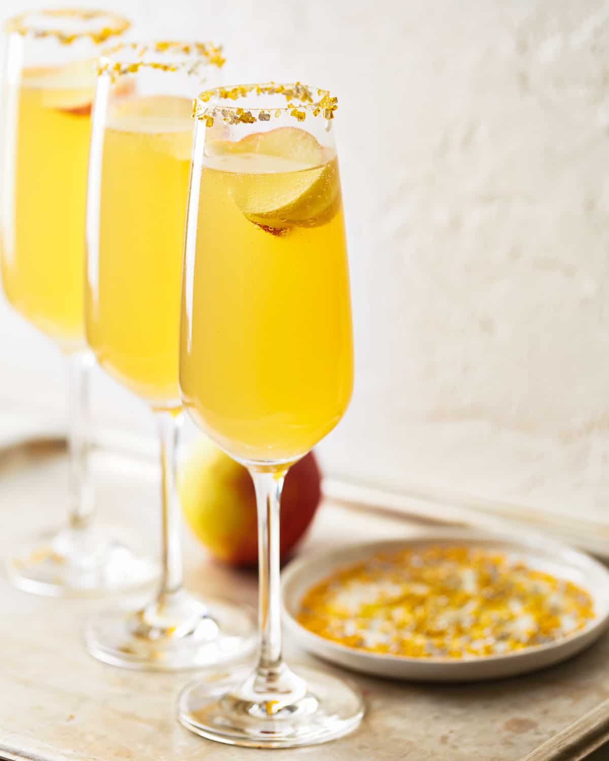 three apple cider cocktails in champagne flutes lined up on a table top