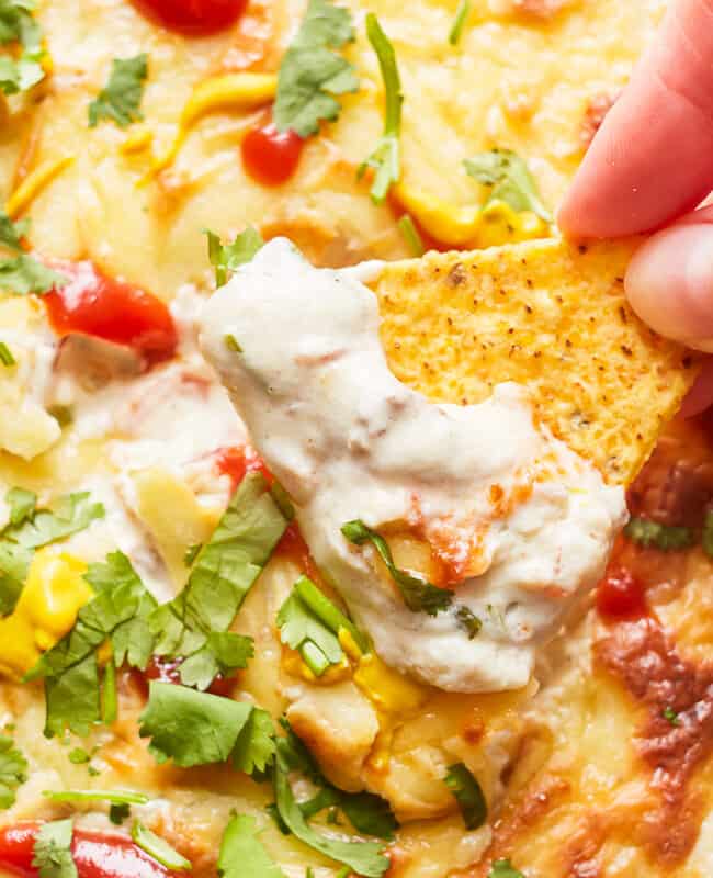 close up of a hand dipping a tortilla chip into cheeseburger dip.