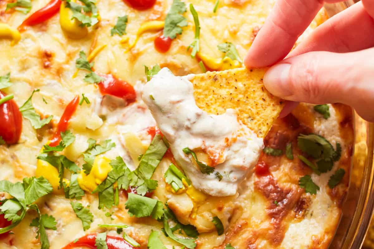 close up of a hand dipping a tortilla chip into cheeseburger dip.