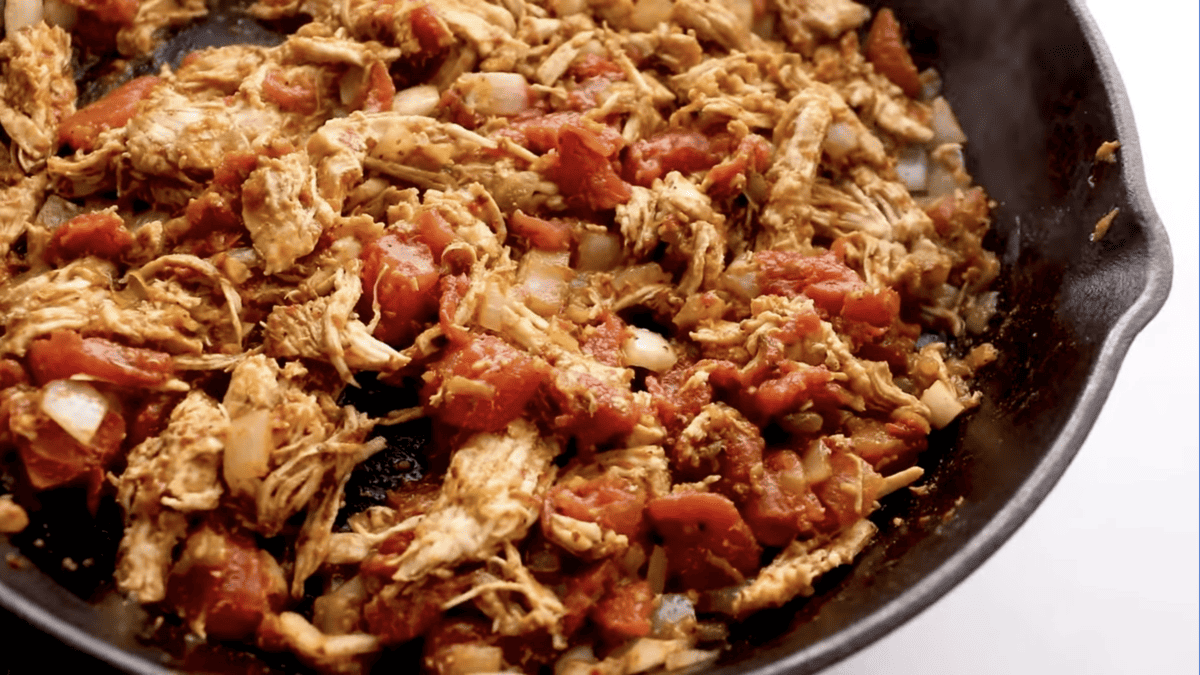 Shredded chicken tacos in a skillet with tomatoes and onions.