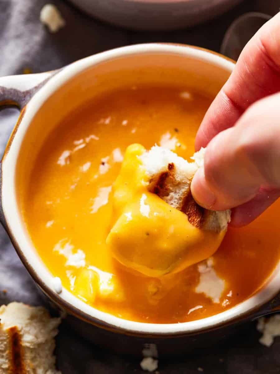 dipping a piece of bread into a bowl of beer cheese soup