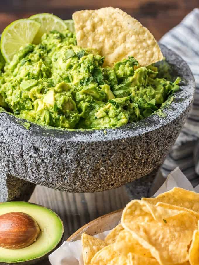 Homemade guacamole dip in a mortar & pestle, with a single tortilla chip dipped in