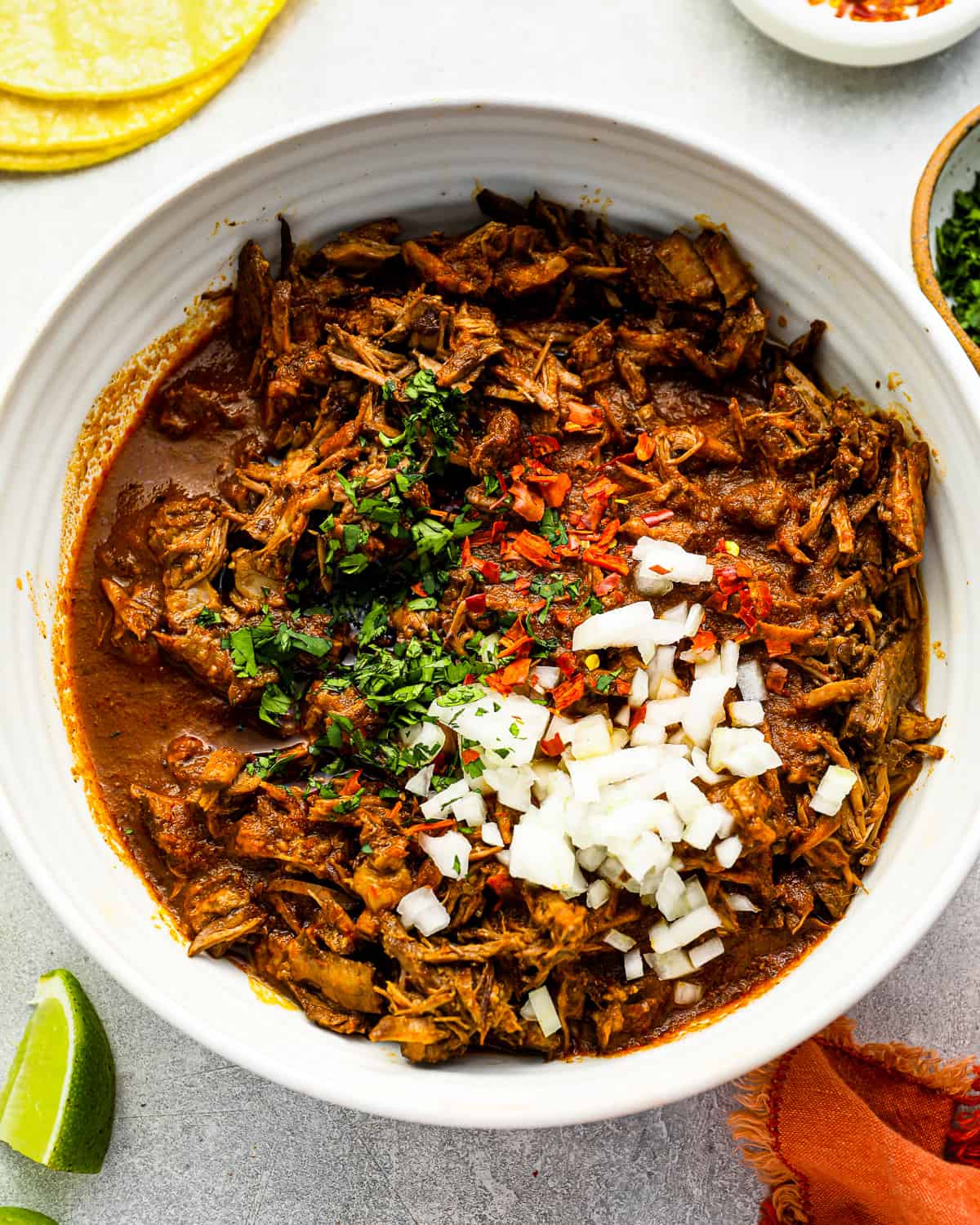 beef birria in a white bowl with limes and tortillas.