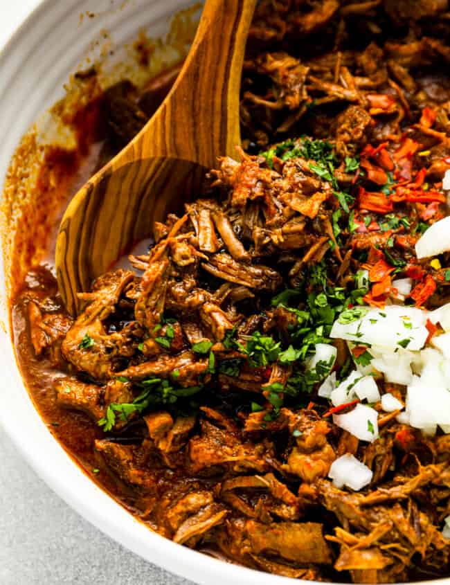 mexican pulled pork in a white bowl with a wooden spoon.