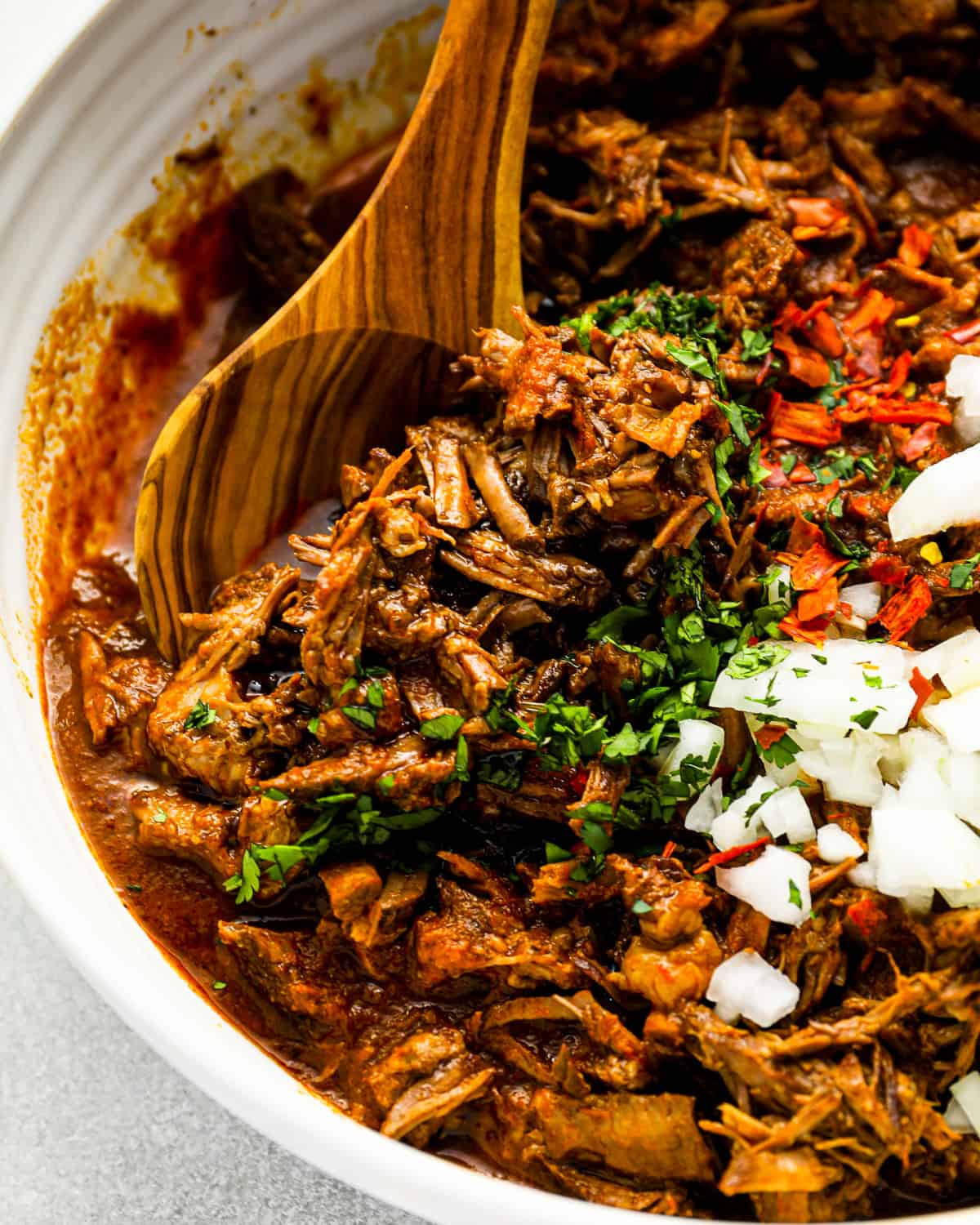 birria meat in a white bowl with a wooden spoon.