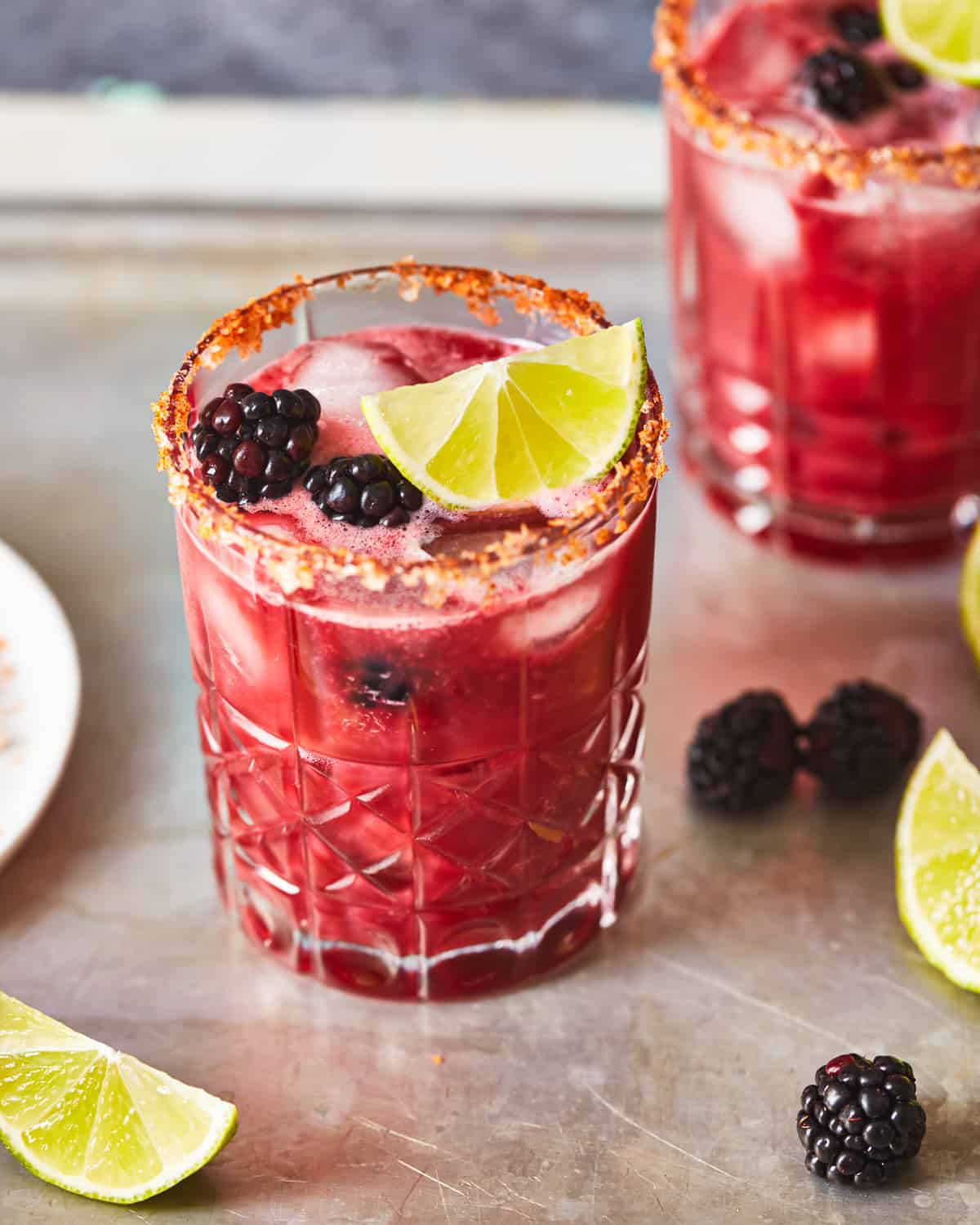 three-quarters view of a blackberry margarita in a short glass with a chili salt rim and blackberry and lime wedge garnish.