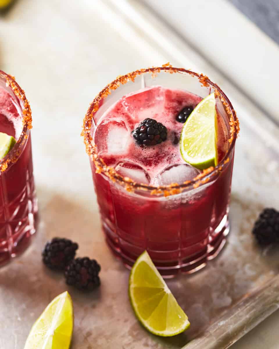 partial overhead view of a blackberry margarita in a short glass with a chili salt rim and a blackberry and lime wedge garnish.