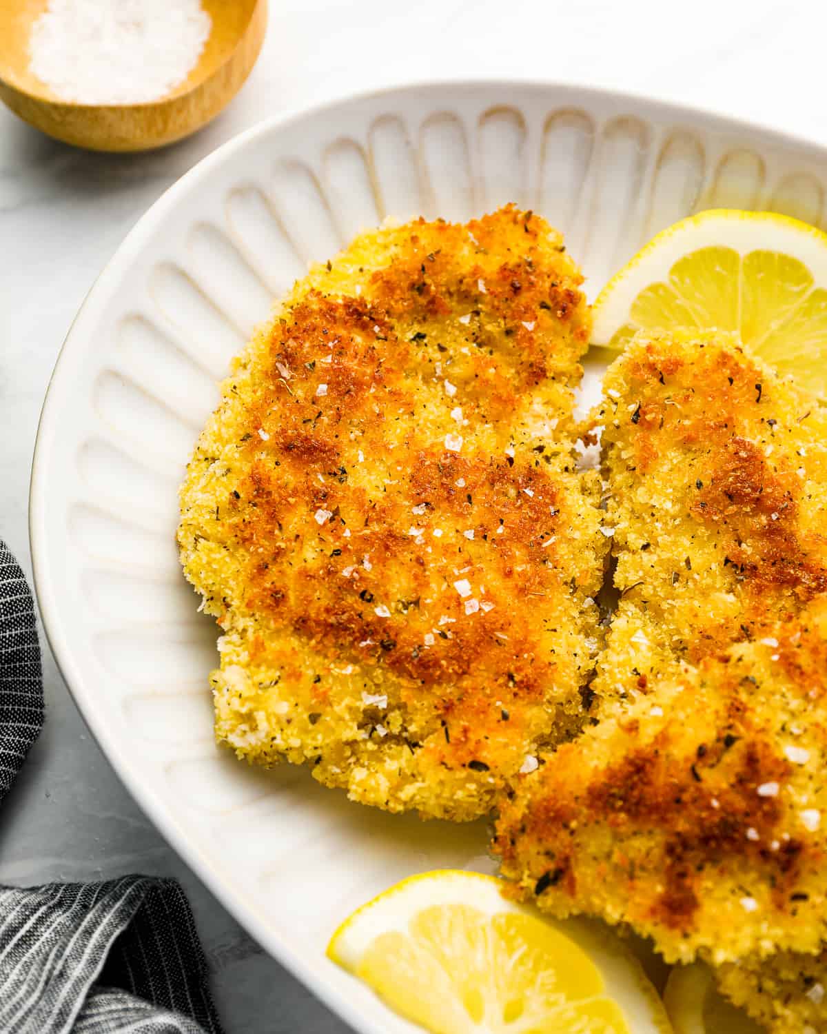 fried chicken cutlets on a white plate with lemon wedges.