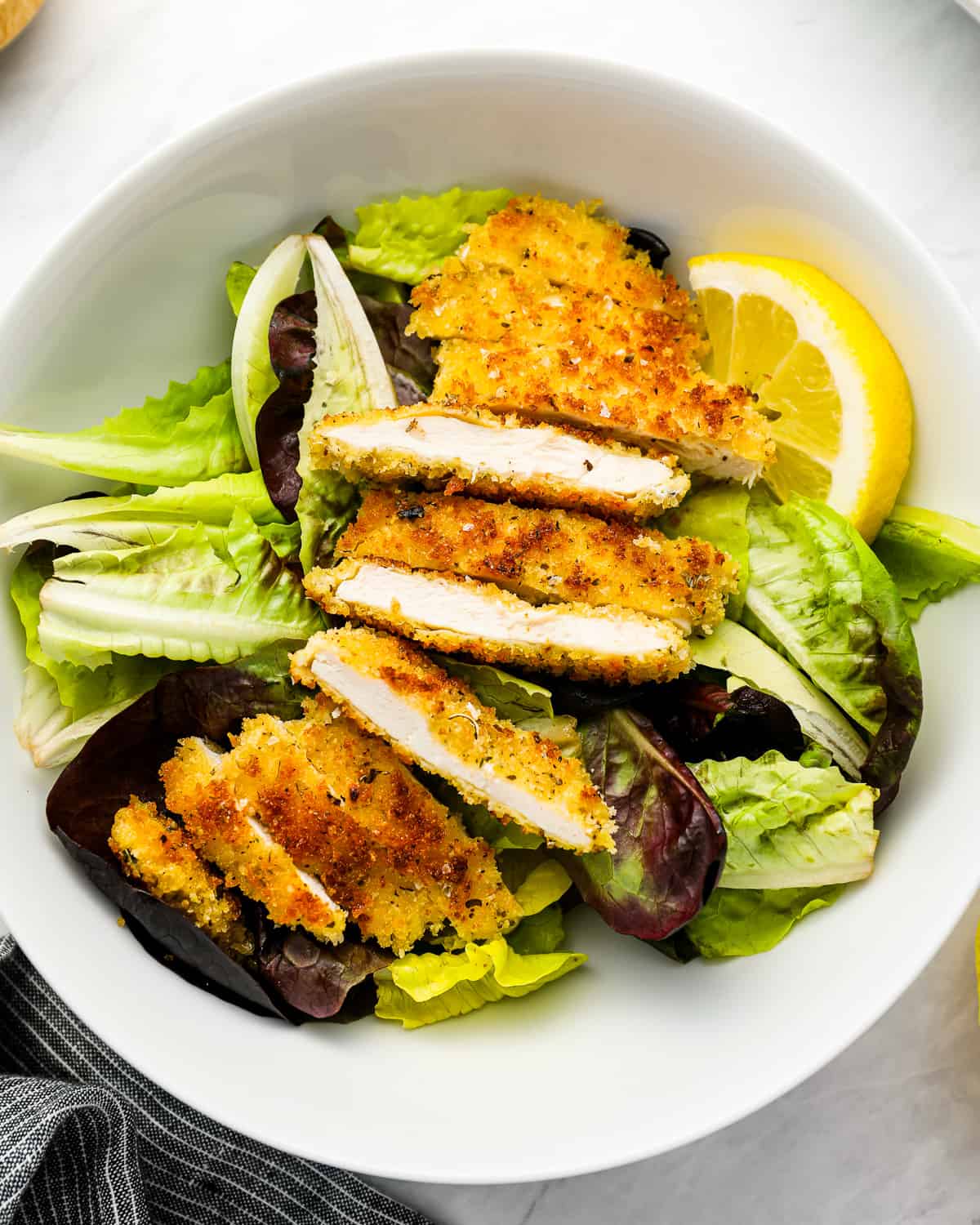 slices of crispy chicken on a bowl of salad.