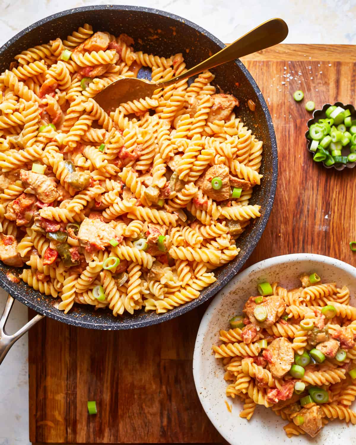 a skillet full of creamy cajun chicken pasta on a tabletop next to a bowl filled with one serving