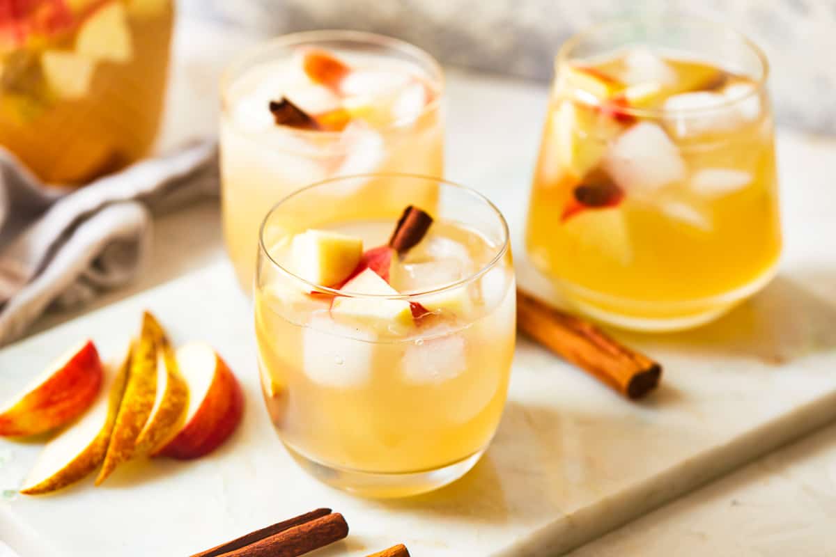 glasses of fall apple sangria on a table top, with apple slices and cinnamon sticks scattered about