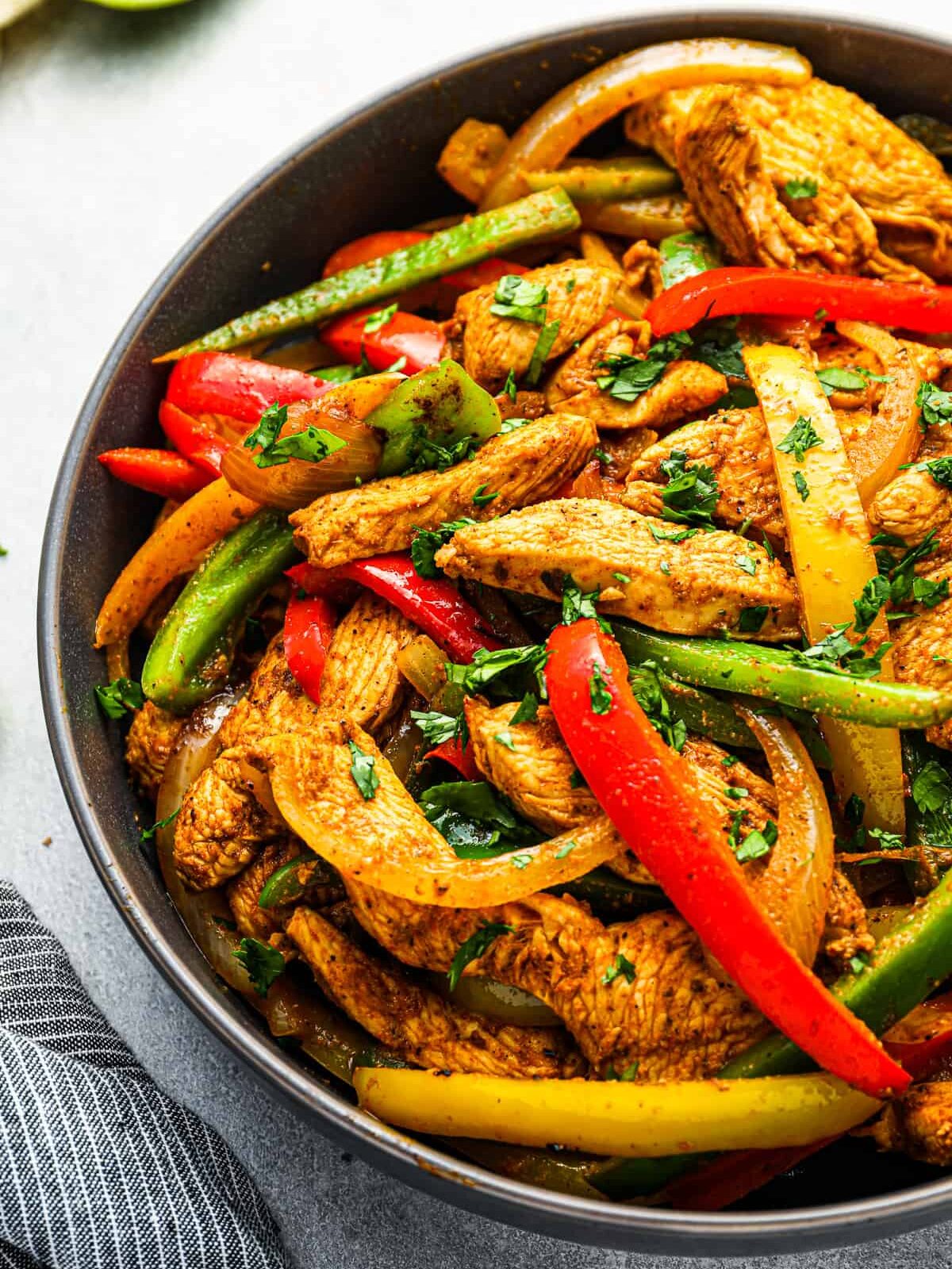 three-quarters view of chicken fajitas filling (strips of chicken and peppers) in a black bowl.