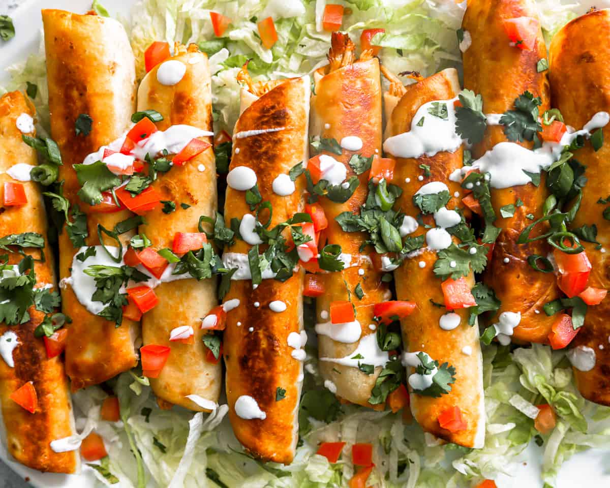 overhead view of 8 crispy rolled chicken tacos on a white oval tray.