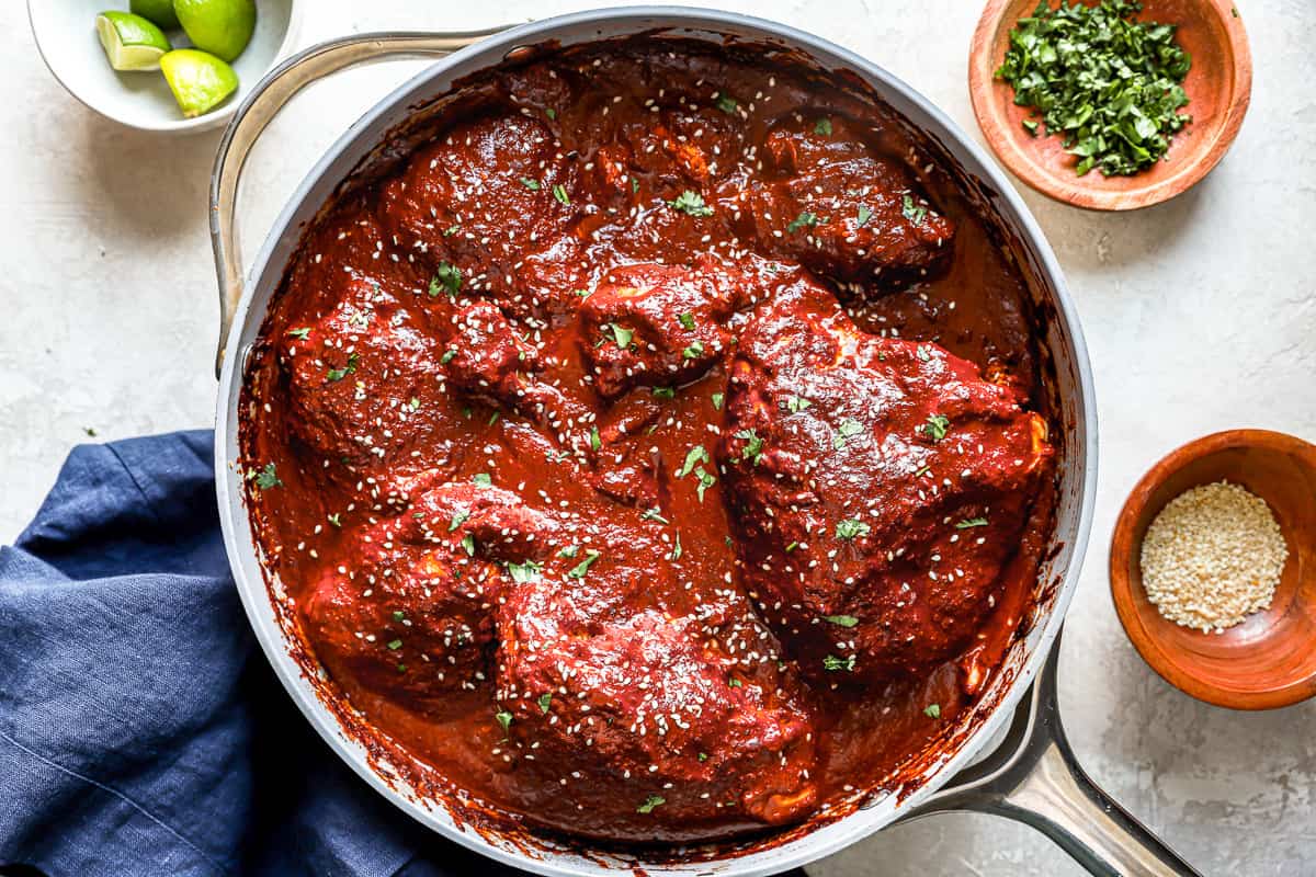 overhead view of chicken cooking in mole sauce, in a stainless steel pan.