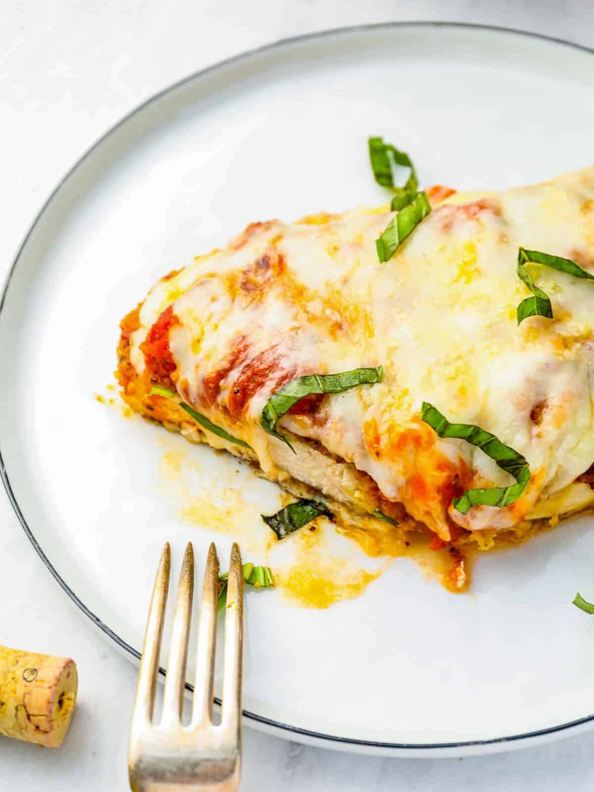 partially eaten chicken parmesan on a white plate with a fork.